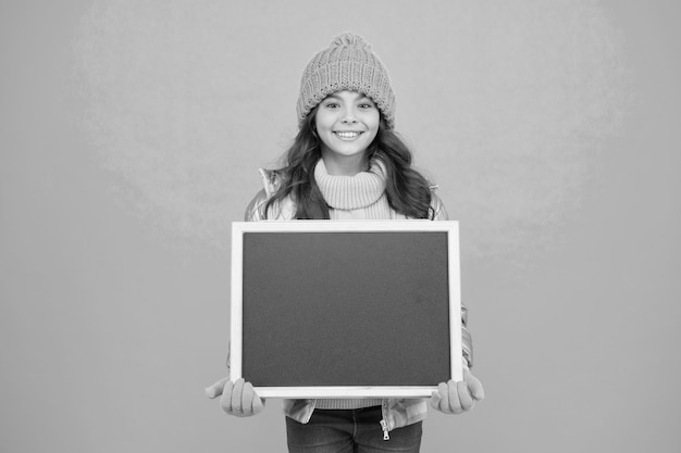 Photo happy holidays show information winter entertainment and activities presentation concept smiling girl wear winter outfit blank chalkboard copy space fresh information information for children