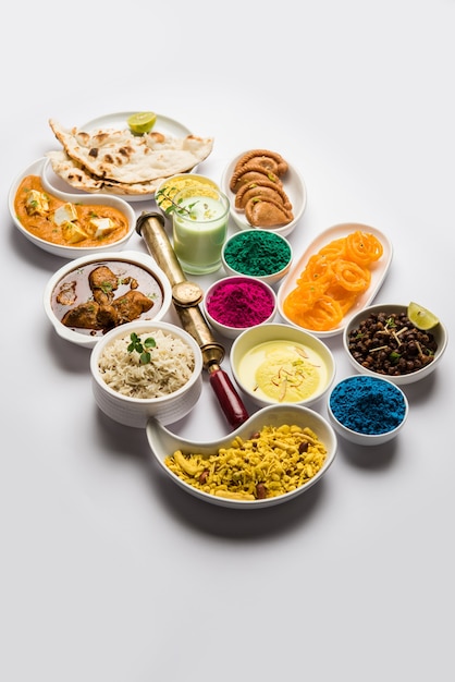 Photo happy holy concept  showing indian assorted lunch food like chicken paneer butter masala naan jeera rice black chana fry jalebi ras malai thandai and farsan with holi colours and pichkari