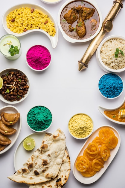 Photo happy holy concept  showing indian assorted lunch food like chicken paneer butter masala naan jeera rice black chana fry jalebi ras malai thandai and farsan with holi colours and pichkari