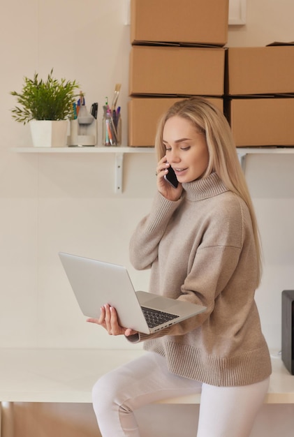 Happy homeowner renter girl using laptop at pile of stacked boxes ordering delivery shipping transpo