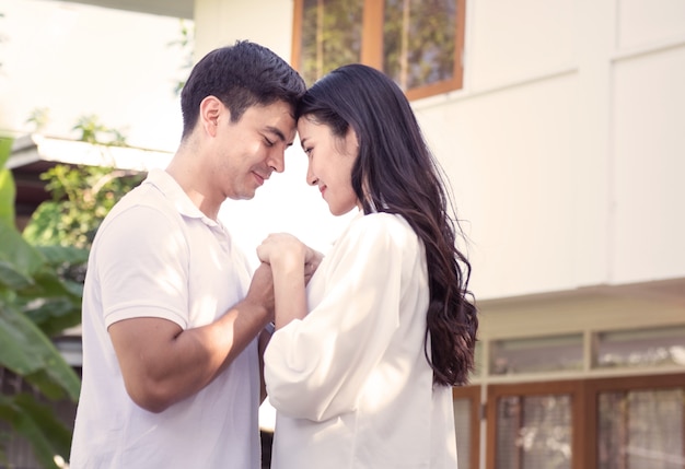 Happy and hopeful caucasian man holding hand asian young woman couple standing at front yard of new home or relocation after leasing or finance concept.