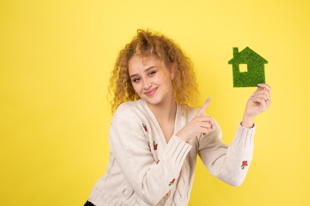 Счастливый покупатель дома Молодая девушка держит в руках модель зеленого дома