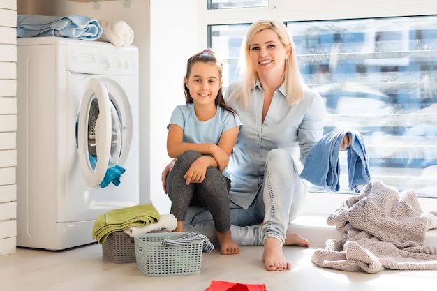 Happy housewife and her daughter with linen near washing machine