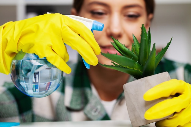 Happy housewife with spray taking care of plants at her home