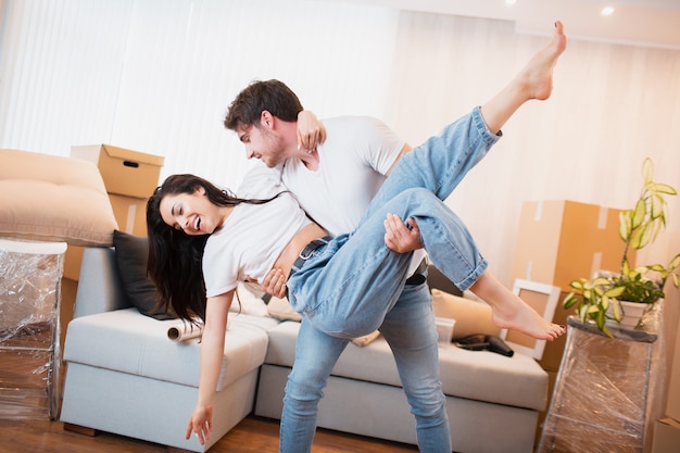 Фото Счастливый муж и жена весело вихрем качаются, перебираясь в собственную квартиру вместе, концепция переезда. обрадованные молодые пары танцуют в гостиной возле картонных коробок, развлекают в день переезда,