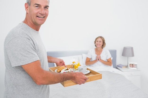 Happy husband bringing breakfast in bed to delighted wife