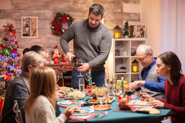 クリスマスの家族のお祝いで彼の妻に赤ワインを注ぐ幸せな夫。