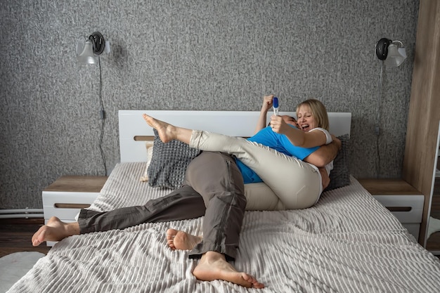 행복한 남편과 아내는 침실에 있는 침대에서 긍정적인 임신 테스트에 기뻐합니다