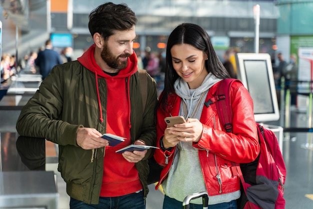 幸せな夫と妻が空港で一緒に立って、スマートフォンでチケットの詳細を確認しますストックフォト