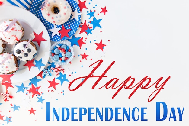 happy independence day, celebration, patriotism and holidays concept - close up of cupcakes or muffins decorated with american flags, donut and red blue candies on plate at 4th july party