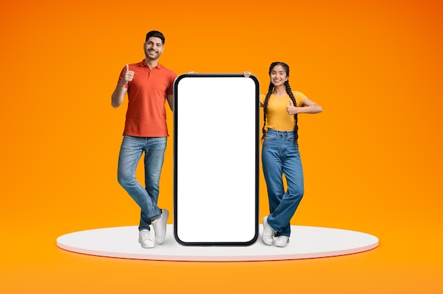 幸せなインド人カップルが大きな白いスマートフォンの近くに立って親指を上げています