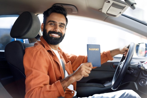 Happy indian driver man showing his passport sitting inside automobile