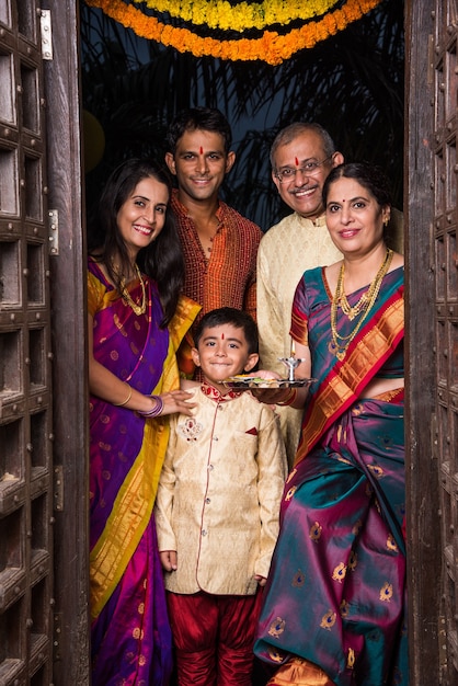 Happy Indian family entering house with puja thali through old antique door - Griha Pravesh or Gruha Pravesh