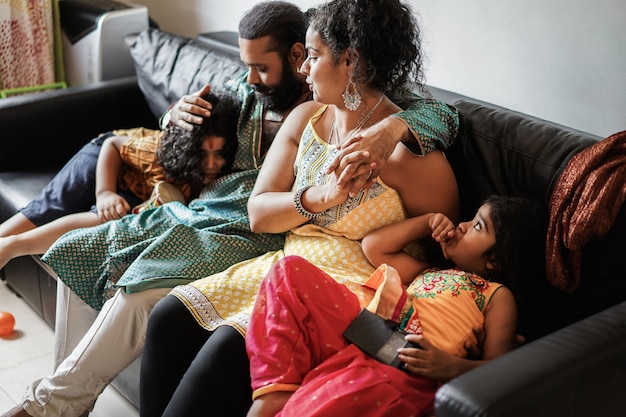 Happy indian family having fun at home sitting on sofa - Focus on mother hand