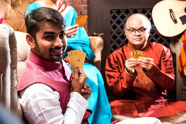 Happy Indian Family playing teen patti or three Cards game on diwali festival night in traditional wear at home