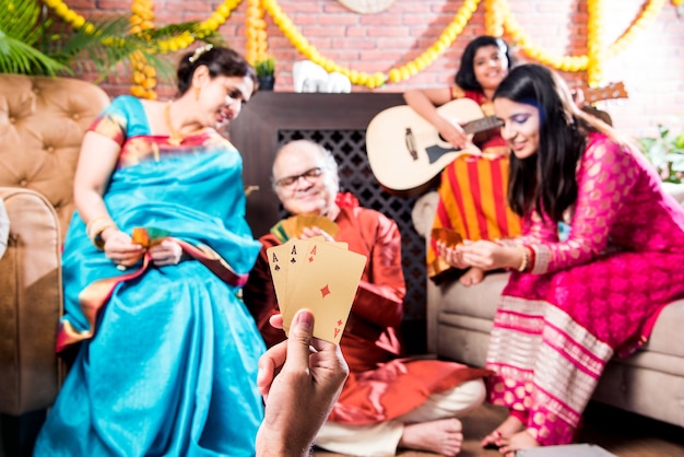 Felice famiglia indiana giocando teen patti o tre carte gioco sulla notte del festival di diwali in abbigliamento tradizionale a casa