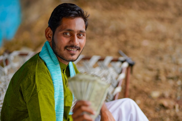 Happy Indian farmer showing money at home.