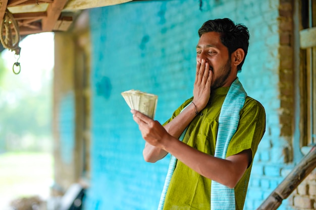 Happy Indian farmer showing money at home.