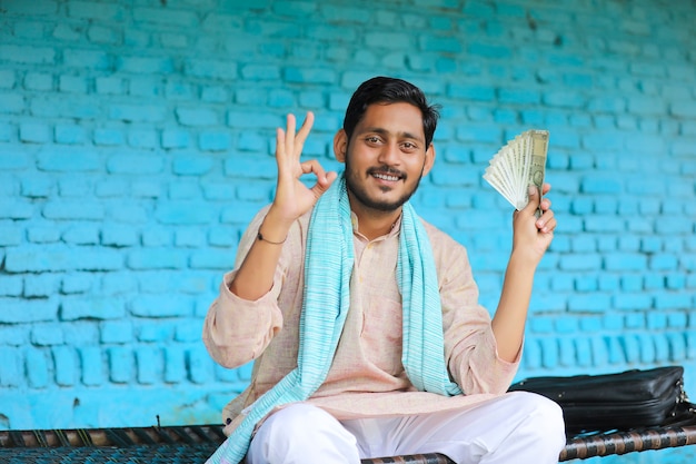 Happy Indian farmer showing money at home.