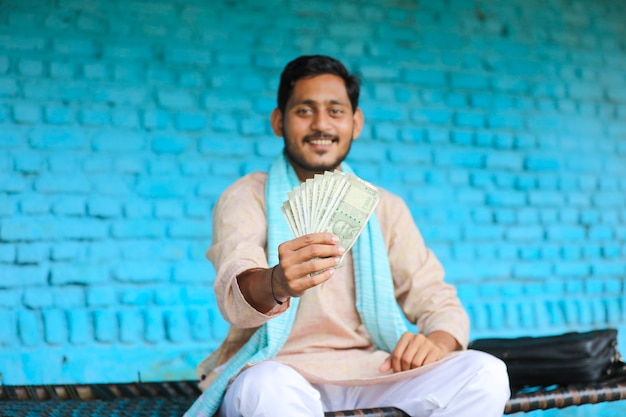 Happy Indian farmer showing money at home.