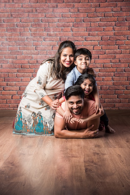 Happy Indian girl and boy playing riding on back or piggyback with father, indoor shot with mother looking