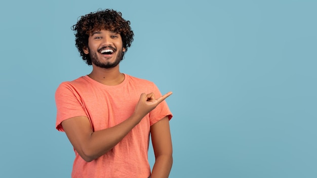 Happy indian guy in pink pointing at copy space