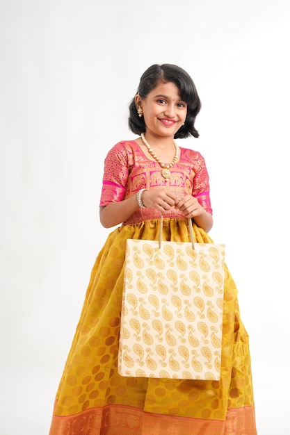 Bambina indiana felice che tiene le borse della spesa su sfondo bianco