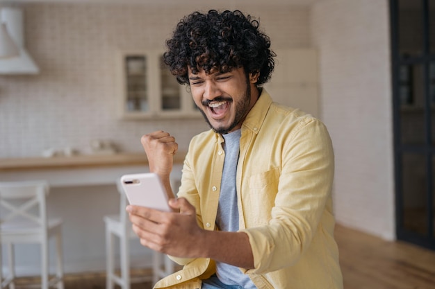 Happy Indian man using smart phone playing mobile game celebration success