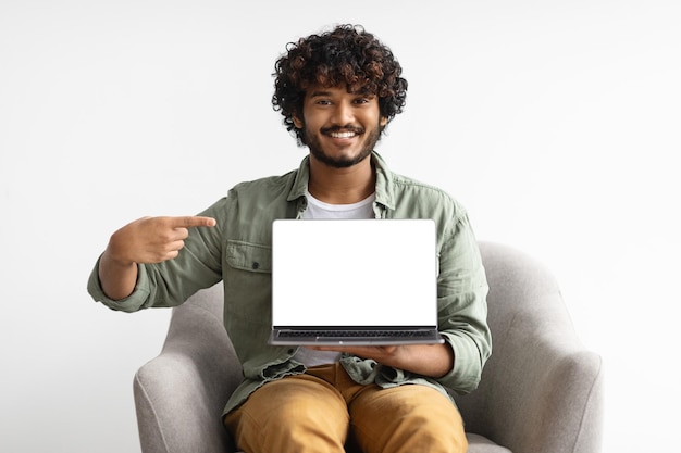 Счастливый индийский мужчина с ноутбуком, указывающим на пустой экран