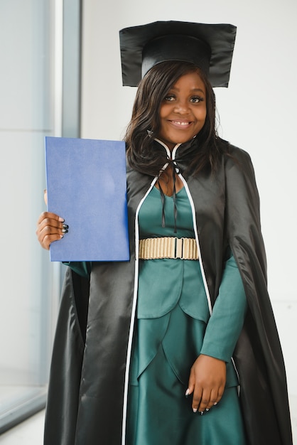 Happy indian university student in graduation gown and cap\
holding diploma certificate. portrait of mixed race asian indian\
and african.
