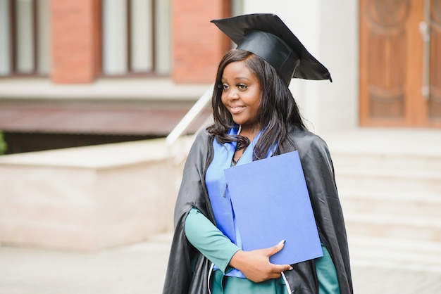 Happy indian university student in graduation gown and cap\
holding diploma certificate. portrait of mixed race asian indian\
and african.