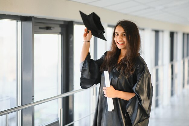 Happy Indian university student in graduation gown and cap holding diploma certificate.