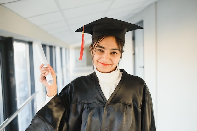 Happy Indian university student in graduation gown and cap holding diploma certificate