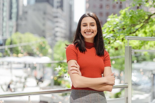 Happy Indian woman with toothy smile looking at camera standing arms crossed on the street