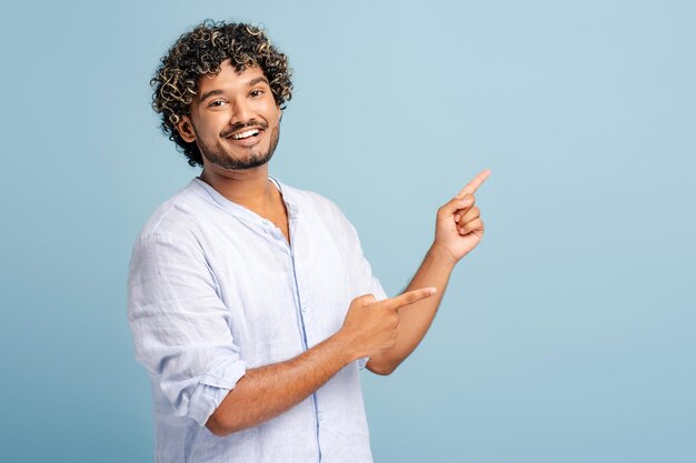 幸せなインド人の若者が青い背景の何かを指さしている
