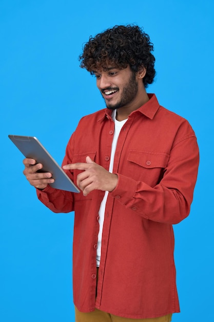 Счастливый индийский молодой человек с помощью цифрового планшета на синем фоне