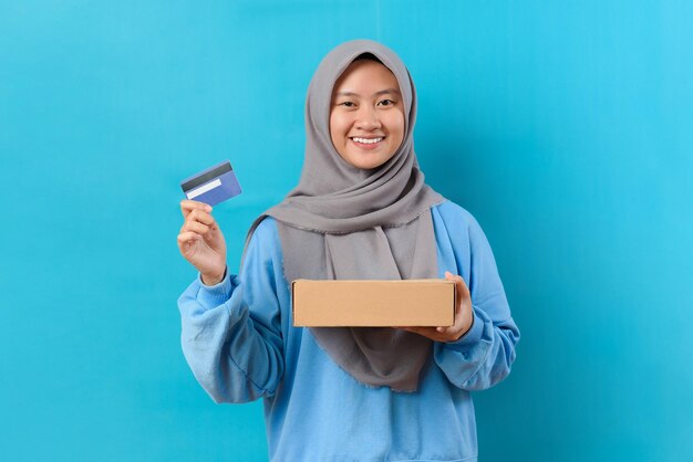 Foto felice donna musulmana indonesiana con hijab che tiene la cassetta dei pacchi e la carta di credito o di debito