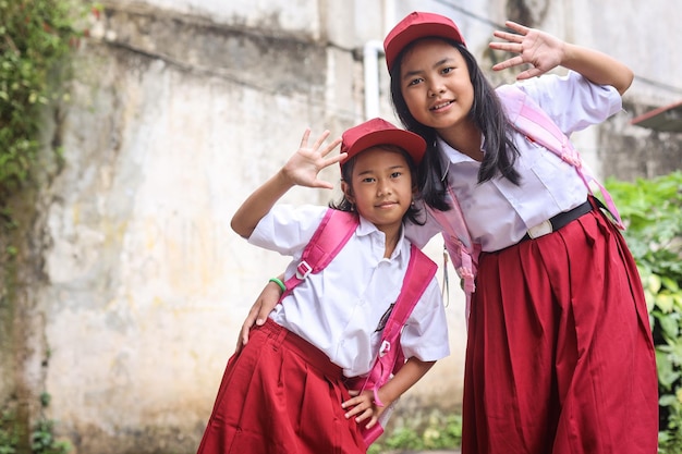 Happy Indonesian schoolgirls of elementary school wearing uniform and backpack waving hand