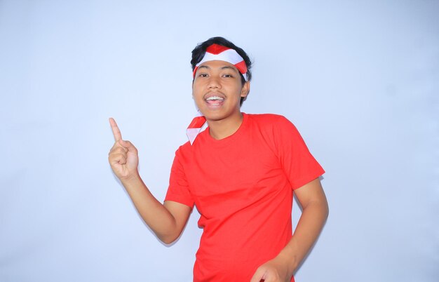 幸せなインドネシアの若者が微笑み、赤いTシャツを着て製品を提示するように指を指している
