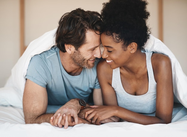 Happy interracial couple bed and intimate morning in relax or bonding relationship at home Man and woman smiling in joyful happiness for love affection or relaxing weekend together in the bedroom