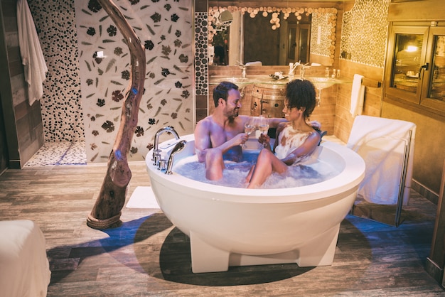 Happy interracial couple relaxed in the jacuzzi enjoying their self and drinking wine