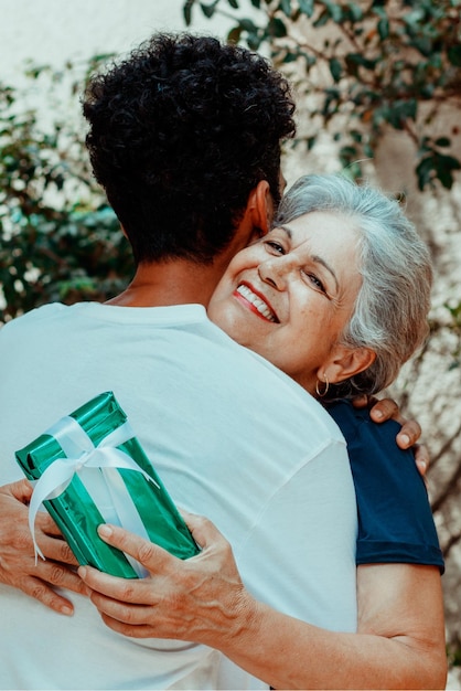 Happy interracial family son gives a gift to his mother in the\
house garden caucasian mother and her black son photo