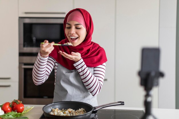 Photo happy islamic woman in hijab recording video while cooking