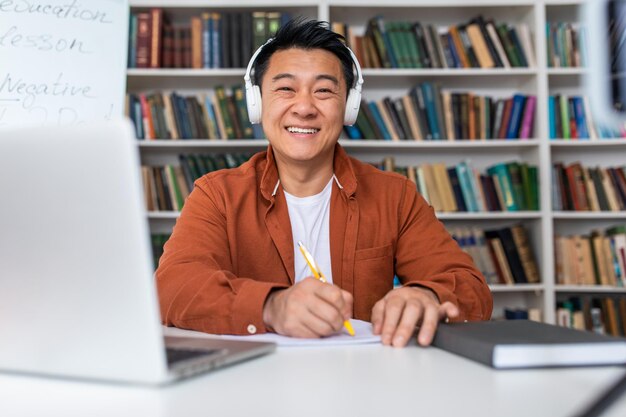 Happy japanese male teacher video calling on laptop at\
workpace