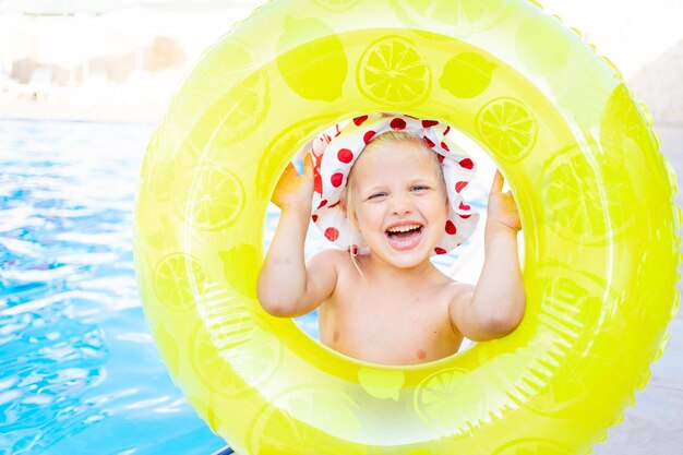 Happy and joyful baby girl looks out of the inflatable yellow circle near the pool in summer and smiles the concept of travel and recreation