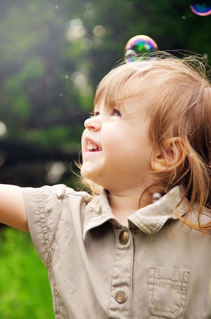 Happy joyful child girl on a sunny summer day against the background of nature and soap bubbles