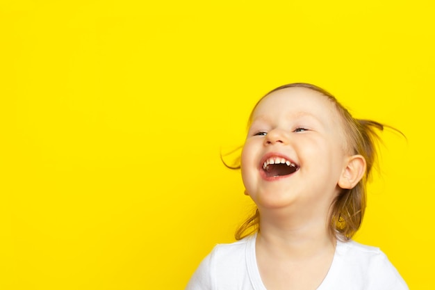 Happy joyful laughter of little girl in white shirt on yellow background