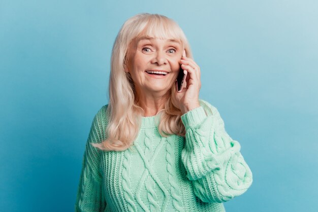 青い背景で隔離のスマートフォンで話している幸せで楽しい成熟した女性