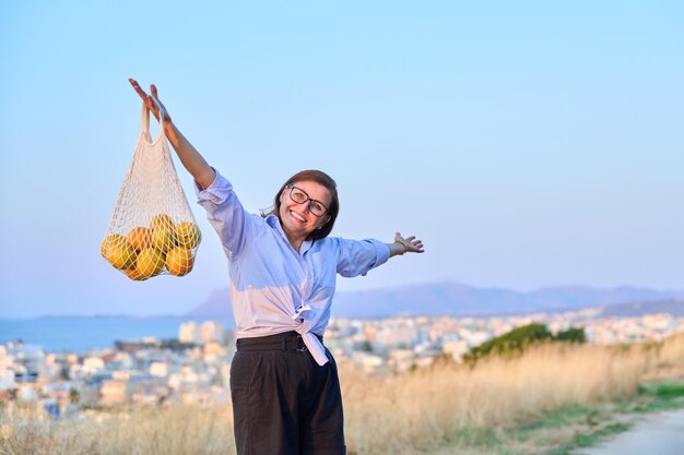 Happy joyful woman with raised hands with grid of oranges blue sky background