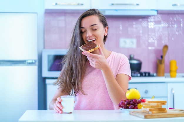 自宅のデザートにナッツチョコレートクリームとトーストのパンを食べて幸せなうれしそうな若い朝食女性